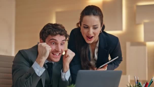 興奮したビジネスチームは ブルーのクローズアップでラップトップ画面を見ながら笑顔で仕事の成功を祝います 契約に署名する勝利を喜んでいる2人のパートナー男性の女性は利益を得ます 同僚は幸せを感じている — ストック動画
