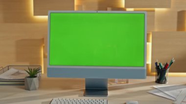 Şirket işyerindeki boş yeşil ekran bilgisayar görüntüsü. Chroma anahtar bilgisayar monitörü modern ofis masasında duruyor. Ahşap masaya yerleştirilmiş şablon modelleme cihazı. İş akışı konseptinde teknoloji 