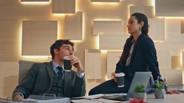 Kahve içen iş çifti yakın planda konuşuyor. Rahatlamış şirket çalışanları dinlenme odasının keyfini bej dolapta kapuçino ile çıkarıyorlar. Gayri resmi ortamda iş arkadaşları eşleri