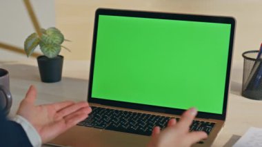 Bilinmeyen kişi çevrimiçi konferansta konuşuyor. Laptop yeşil ekranı kapalı mekanda görüyor. Ofisteki Chroma Key bilgisayarında tanımlanamayan yönetici projesini sunuyor. Model aygıtı kullanan işçiler 