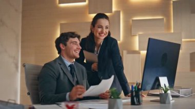 Mutlu meslektaşlar ofisteki bilgisayarları videoya çekiyorlar. Gülümseyen işadamı elinde yeni projeyi gösteren belgeler tutuyor. İş adamı görünümlü bilgisayar monitörü konferans görüntülü konuşmayı içeride yapıyor 