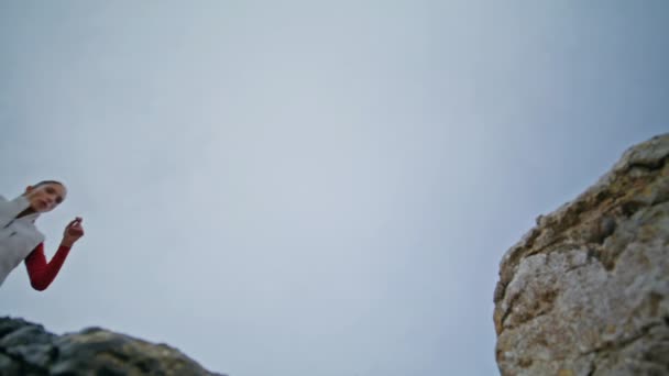曇りの空の背景下のビューで自然石の上を走っているアクティブな女性 毎日のトレーニングで強さを示すボールダーにジャンプする赤いレギンスのダイナミックランナー エネルギーガールは身体活動を楽しむ — ストック動画