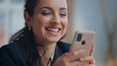 Akıllı telefon kullanan genç bir iş kadını kreatif ajansın kapanış çekiminde oturuyor. Mutlu gülümseyen kadın internet sörfü modern telefonla eğleniyor. Ofis yöneticisi cep telefonuna göz atıyor