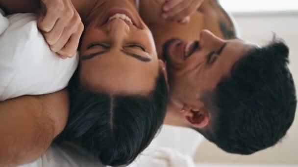 笑着新婚夫妇在床上玩的很开心 微笑的男人吻着积极的女人的肩膀在舒适的卧室垂直的视野 在家庭氛围中拥抱的性感夫妻 男朋友和女士的关系 — 图库视频影像