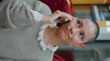 Modern yüksek hızlı trende konuşan ciddi bir hippi. Yaklaş. Endişeli kısa saçlı kadın akıllı telefondan konuşuyor vagon dikey videosu. Modayı takip eden kız yolcu kalkışı bekliyor..