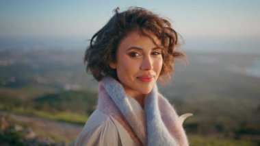 Güzel sonbahar sahillerinde manzaralı günbatımına bakan düşünceli bir kadın portresi. Serene gezgin tatil akşamında deniz manzarası güzeline yakından bakıyor. Kıvırcık esmer sakin tepenin üstünde duruyor.