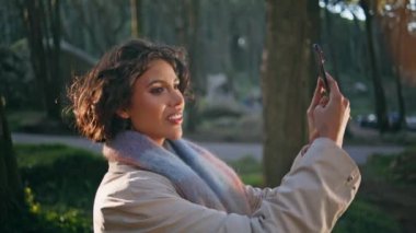 Gülümseyen kız akıllı telefonda doğa manzarasını fotoğraflıyor mutluluk saçıyor. Mutlu kadın gezgin cep telefonuyla canlı orman doğasını çekiyor. Kadın blogcu yolculukta ormanı filme alıyor.
