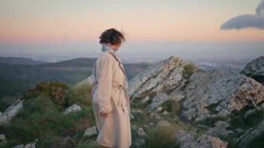 Alacakaranlıkta dağ yolunda şık bir ceketle yürüyen bir turist. Sonbahar tatilinde kayalık araziyi keşfeden zarif kadın gezgin. Gülümseyen kadın kaşif akşam vakti çimenli tepelerde geziniyor..