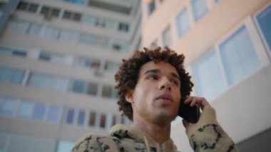 Hafta sonu gezintisinde akıllı telefondan konuşan Latin bir adam. Şehirdeki yüksek binalarda telefonla konuşan kıvırcık, mutlu bir adam. Havalı hipster dostça iletişimin keyfini çıkar..