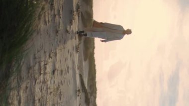 Huzurlu kadın kumullarda dikey yürüyor. Sakin model siluet, deniz kenarında güneş ışığında gezinirken keyif çatıyor. Afro-Amerikan tarzı. Doğaya hayran olan tek başına düşünen. Meditasyon eğlencesi.