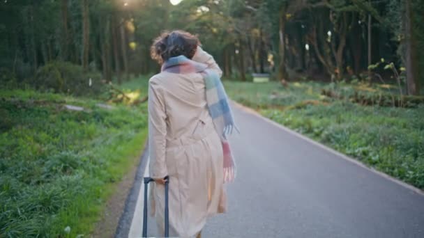 旅を体現するスーツケース付きの美しいワンダーウォーク林道 静かな朝に木の道を散策するスカーフのシックな女性は ワンダルームを象徴しています ファッショナブルなエクスプローラーは休日の旅行を楽しむ — ストック動画