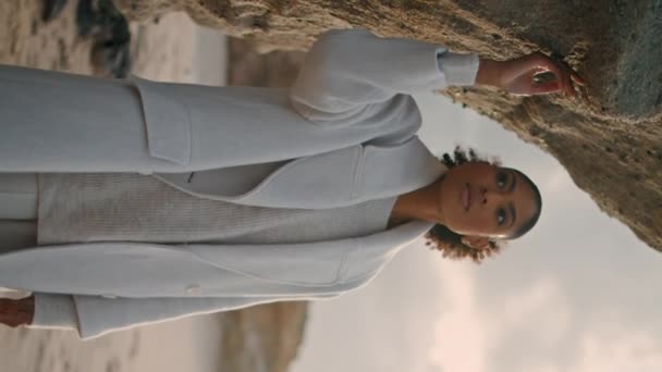 空のビーチの垂直に崖の壁に触れる美しい少女 セリーン アフリカ系アメリカ人は自然を賞賛するのが好きだ 人生を考える穏やかな黒髪モデルは 屋外にインスピレーションを与えます 安静な女性 — ストック動画