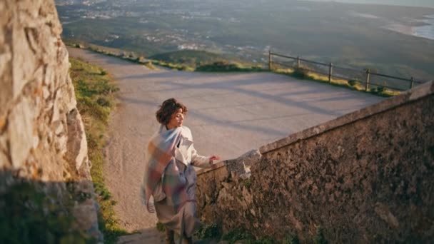 柔らかい夜の日差しで文化的なランドマークの階段を登るアドベントゥロウスの女性 日没の光で入浴した沿岸の丘の上の目的地を探してリラックスした旅行者 美しい女の子は絵のような自然を楽しむ — ストック動画
