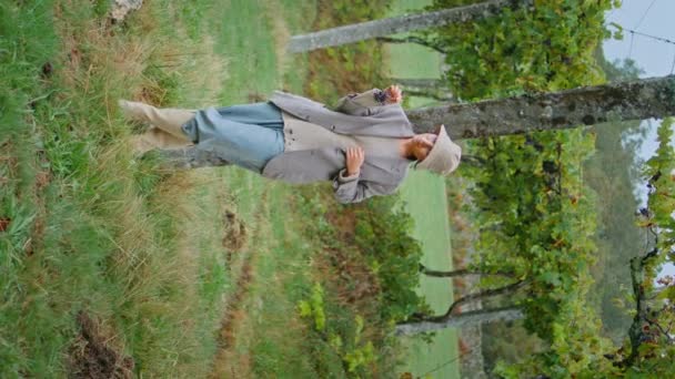 葡萄园工人穿着睡衣在绿色种植园休息 松驰的年轻女子站在青草上吃成熟的新鲜葡萄垂直视频 时尚的女孩品尝着多汁的浆果 享受着秋天的一天 — 图库视频影像