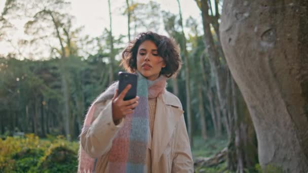 カジュアルな秋のスタイルのクローズアップを着た森でスマートフォン信号を検索する女性 ポートレート美しいブルネットは 夜の森林で接続を見つけるために携帯電話を上げます 混乱した少女のブラウジング電話 — ストック動画