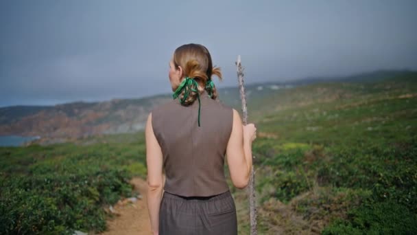 孤独なリアビューで独立したハイカーウォーキングパス 曇りの日にスティックで丘を散策するブレードを持つ夏の少女 静かな自然のトレイルで未知の旅行者トレッキング 野生の風景の旅 — ストック動画