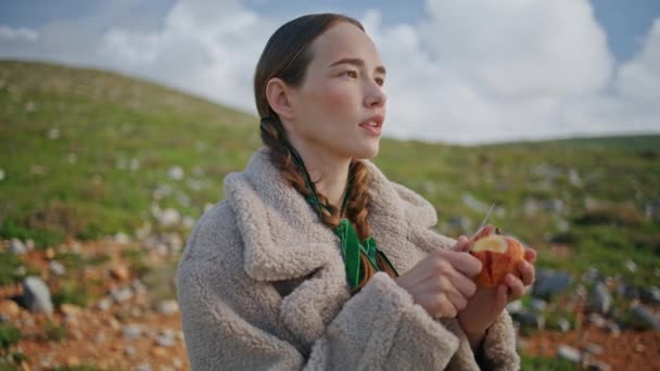 在青山上剥苹果的女装 在外衣上忙碌的旅行者在户外享受着健康的小吃 和平的女人欣赏大自然 在旅程中结出果实 环境友好型生活方式 — 图库视频影像