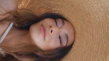 Hasır şapkalı kız şehire gülümseyen yüz portresiyle poz veriyor. Muhteşem esmer model kamera şehirde dikey olarak güneş ışığının tadını çıkarıyor. Yaz bulvarında dinlenen genç bir kadın dik dik bakıyor..