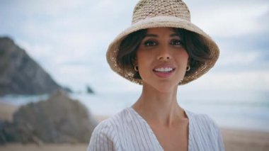 Sahilde kameraya bakan gülümseyen kadın portresi. Çekici seyahat kızı okyanusta yaz tatilinin tadını çıkarıyor. Kumlu deniz kıyısında poz veren mutlu muhteşem bayan. Kayalık ada kıyısında rahat bir turist.