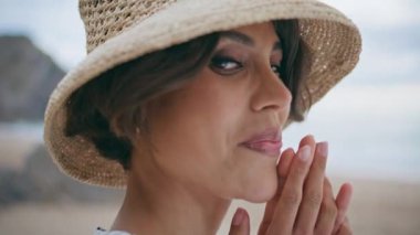 Tatil portresi üzerinde dinlenen mutlu kız. Gülümseyen güzel kadın yazın okyanus esintisinin tadını çıkarıyor. Çekici turist görünümlü kamera ada sahilinde hasır şapkanın altında saklanıyor..