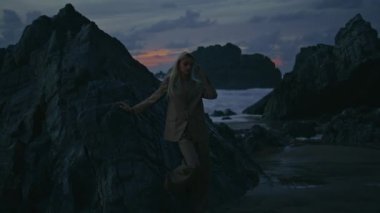Profesyonel model gece karanlığında poz veriyor. Akşamları Rocky Sahili 'nde lüks ve seksi bir kıza ışık tutuyor. Moda güzeli kadın reklam için çekim yapıyor bulutlu alacakaranlık gökyüzüne yaslanmış kayalar..