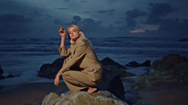 여자는 하늘에서 바위를 모델링 바위에 해변을 저녁에 우아한 정장에 매력적인 — 비디오