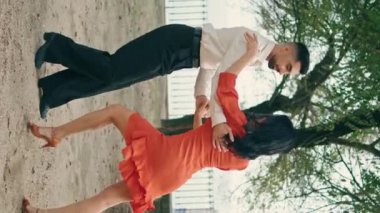 Şehir parkında yaz günü dans eden tutkulu Latin çift. Dikey mutlu enerjik çift dışarıda salsa yapıyor. Kırmızı elbise giyen güzel esmer kadın ağır çekimde hareketlerin tadını çıkarıyor..