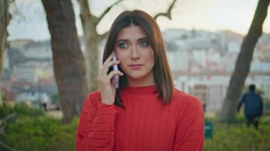 Güneşli şehir parkında cep telefonunu arayan endişeli bir kadın. Kırmızı elbiseli güzel, üzgün kadın yeşil bahçedeki akıllı telefondan konuşuyor. Esmer kız cep telefonuyla konuşuyor. 