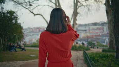 Kırmızı elbiseli kadın tek başına parkın arkasına bakıyor. Esmer, genç model, şehir manzaralı bahçede geziniyor. Çekici, rahat, saçlarına dokunan kız hafta sonu sakin bir yürüyüş yapıyor. Halk yaşam tarzı konsepti