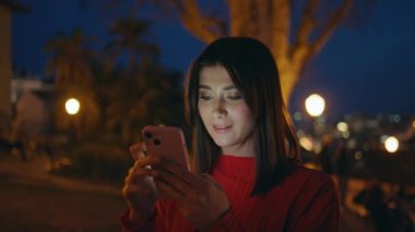 Göz kamaştırıcı turist kız cep telefonuna mesaj atıyor. Gece görüş mesafesinde. Modern akıllı telefonu elinde tutan çekici, rahat bir kadın. Akşamları yalnız başına bekleyen bir arkadaşıyla buluşuyor. Aydınlanmış park. Gece hayatı konsepti 