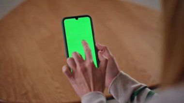 Yeşil ekran cep telefonu uygulamasını inceleyen bir kız apartman masasını kapatıyor. Kadın elleri evde krom tuşlu akıllı telefona dokunuyor. Yeşil ekran cep telefonu kullanan tanınamayan serbest çalışan.