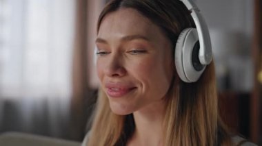 Kulaklıklı gülümseyen bir kadın. Hafta sonu internette dizüstü bilgisayar yazıyor. Rahatlamış serbest çalışan kulaklıkla müzik dinleyen kanepe kapanışında çalışan bir bilgisayar. Mutlu öğrenci çevrimiçi çalışıyor.