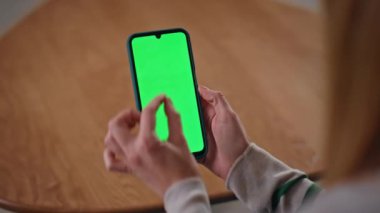 Ofiste parmakları yakınlaştıran akıllı telefon, yakın plan. Sosyal medya içeriğini yeşil ekran cep telefonundan izleyen tanınmayan bir kadın. Bilinmeyen serbest çalışan dairede krom anahtara dokunuyor