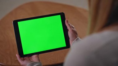 Uzak bir iş yerinde krom anahtar tabletine benzeyen tanınmayan bir kız. Kadın elleri yeşil ekranlı bilgisayarı tutarak sosyal medyayı izliyor. Mockup Gadget 'tan Meçhul Kadın Bağımsız Video çağrısı.