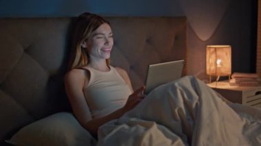 Gece geç saatlerde, rahat bir yatakta tablet ekranda film izleyen bir kız. Gülümseyen rahat kadın yatma vakti bilgisayardaki komik videodan zevk alıyor. Karanlık yatak odasında uyumadan önce çevrimiçi mutlu güzel bayan mesajları.