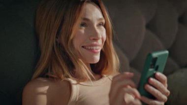 Sabah kızı rahat bir yatakta uyandıktan sonra cep telefonu mesajını okuyor. Gülümseyen güzel bir kadın akıllı telefonuyla yatak odasını geriyor. Mutlu gevşemiş bayan Tembel güneşli hafta sonunun tadını çıkar.