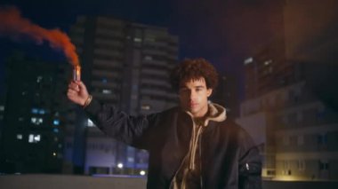 Gece geç saatlerde, elinde kırmızı el bombası tutan bir adam. İspanyol adam gece binalarının yakınında renkli dumanlar yakıyor. Sokakta duran kameralı, renkli bombalı genç, kıvırcık hippi. Protesto kavramı