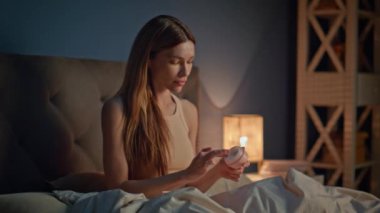 Yüzüne nemlendirici krem süren bir kadın rahat bir dairede uyumaya hazırlanıyor. Rahatlamış gülümseyen kız yatmadan önce yüz derisini besleyici kozmetiklerle nemlendiriyor. Güzel bayan akşamları cilt bakımı yapar..