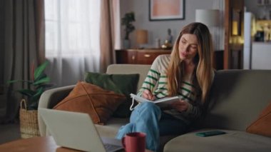 İnternette kurs yazan kız evdeki kanepeye dizüstü bilgisayar bakıyor. Bilgisayarda video dersi dinleyen mutlu kız öğrenci, not defterine not tutuyor. Sakin kadın serbest çalışan uzak istemciyle iş görevini tartışıyor