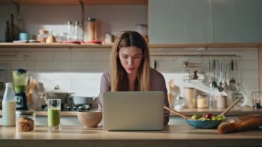 Ev hanımı dizüstü bilgisayarla mutfakta internetten video tarifi arıyor. Daire mutfağında uzaktan çalışan gülümseyen serbest çalışan bir kadın. Evde internetten bilgi arayan mutlu kız öğrenci.