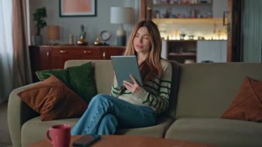 Ev kanepede kitap okuyan kadın. Tabletten e-posta alan, gülümseyen, rahat, hayalperest bir kadın. Çekici, mutlu ev hanımı. İnternetten bilgisayar alıyor. Koltukta rahat bir şekilde oturuyor.