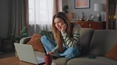 Kız videosu konforlu oturma odasında dizüstü bilgisayar arıyor. İnternette arkadaşlarıyla sohbet eden gülümseyen bir kadın bilgisayar kamerasıyla evde oturuyor. Neşeli dişiler uzak iletişimin tadını çıkarırlar..