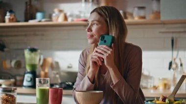 Ev hanımı cep telefonunda SMS okuyor hafta sonu kahvaltısı yapıyor. Romantik kadın mutfak tezgahında akıllı telefon ekranı gibi duruyor. Gülümseyen mutlu kız cep telefonuyla online sipariş veriyor..