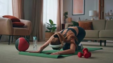 Spor kadını sabah antrenmanında kulaklık takarak vücut esnekliğini geliştiriyor. Modern oturma odasında spor paspası üzerinde egzersiz yapan zayıf genç bir kadın. Spor fitness kızı dairede kaslarını esnetiyor..