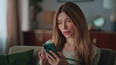 Oturma odasındaki cep telefonunda bankacılık uygulamasına göz atan ciddi bir kadın. Sakin genç bayan, kanepede akıllı telefon ekranı haberlerine bakıyor. İnternette sörf yapan çekici serbest yazar..