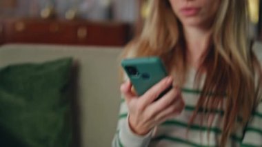 Evde cep telefonuna benzeyen şaşkın bir kız var. Yakın plan. Akıllı telefondan etkileyici haberler okuyan genç bir kadın koltukta oturuyor. Duygusal iş kadını kredi ödeme hatırlatmaları alıyor