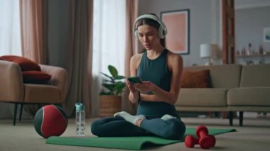 Yoga yapan kadın evde nilüfer nilüfer pozisyonu için müzik aleti açıyor. İnternette meditasyon dinleyen kulaklıklı sakin bir kız spor minderinde oturuyor. Güzel bayan sabah zihin dengesi hisseder..