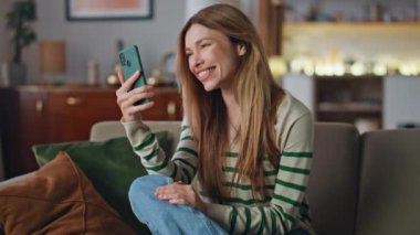 Neşeli kız cep telefonunu arıyor oturma odasındaki kanepeyi kapatıyor. Akıllı telefon web kamerasında konuşan heyecanlı güzel bir kadın çevrimiçi toplantının tadını çıkarıyor. Gülümseyen bayanın internet konferansı var..