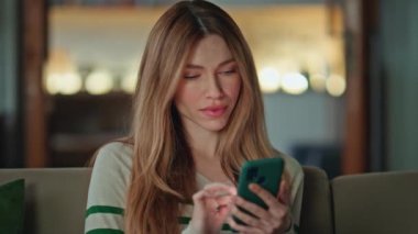 Samimi kanepede SMS akıllı telefonu okuyan gülümseyen bir kadın. Çekici bir kız cep telefonu başvurusunda internetten alışveriş yapmayı seçiyor. Cep telefonundan sosyal medyayı izleyen mutlu, rahat bayan..