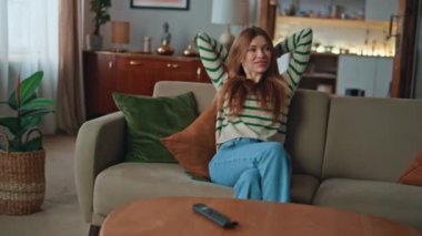 Tasasız kız modern oturma odasında dinleniyor. Akıllı telefondan mesaj alan mutlu kadın. Cep telefonunda SMS okuyan gülümseyen bayan rahat koltukta oturuyor. Hafta sonu eğlence konsepti.